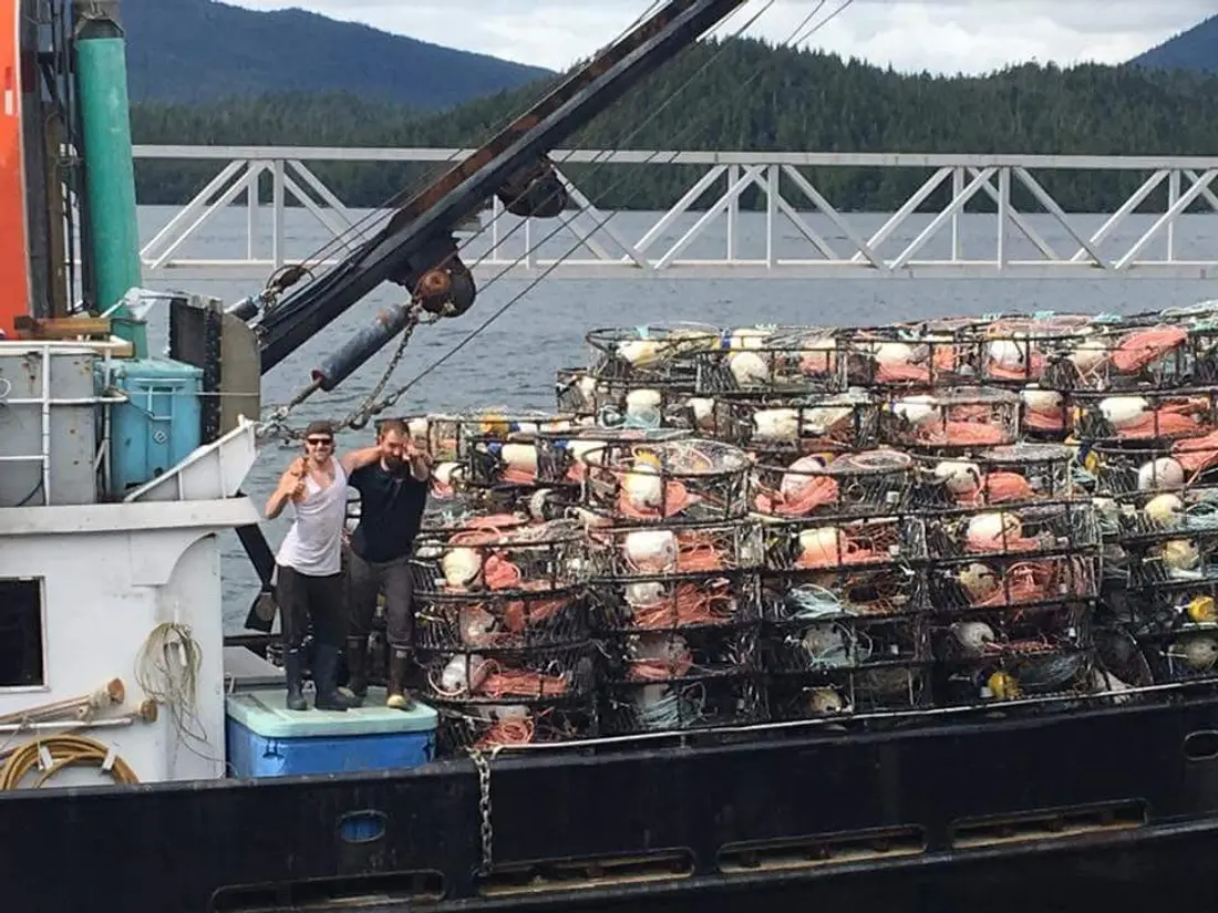 Two crew members standing beside a towering stack of crab traps on the boat.