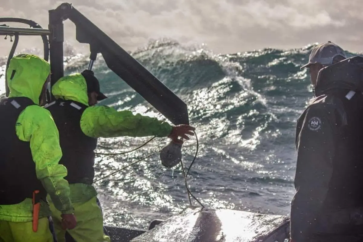 Crew in foul-weather gear working a winch as a heavy swell breaks off Hecate Strait.